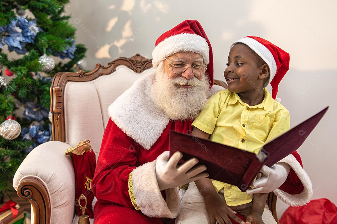 Papai Noel lendo um livro de histórias para uma criança no colo. Educação