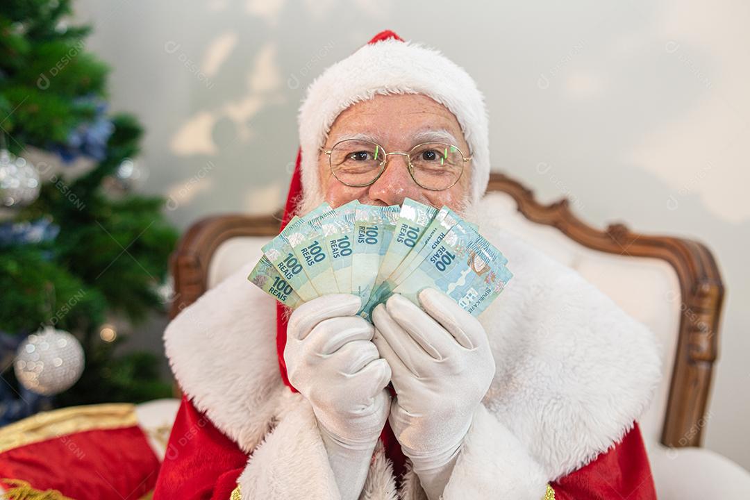 Papai Noel contando contas de dinheiro brasileiras. Notas reais. 100 Reais