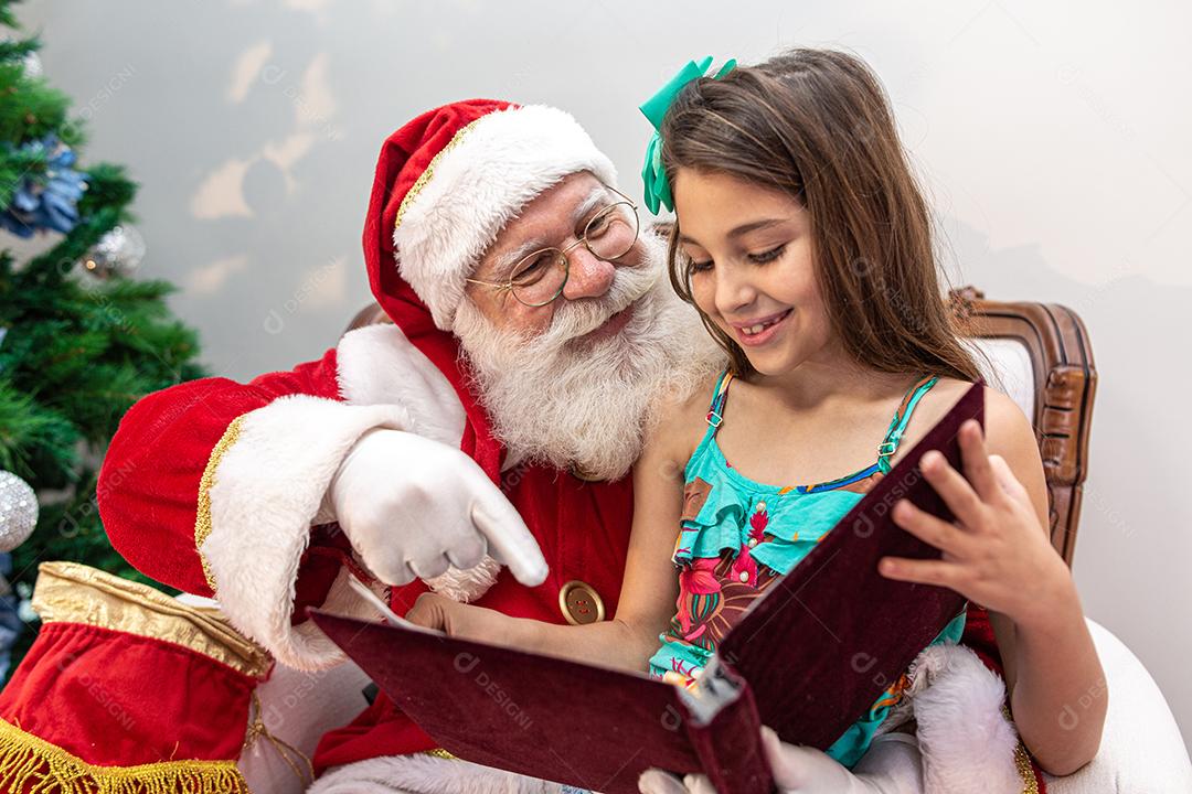 Papai Noel lendo um livro de histórias para uma criança no colo. Educação