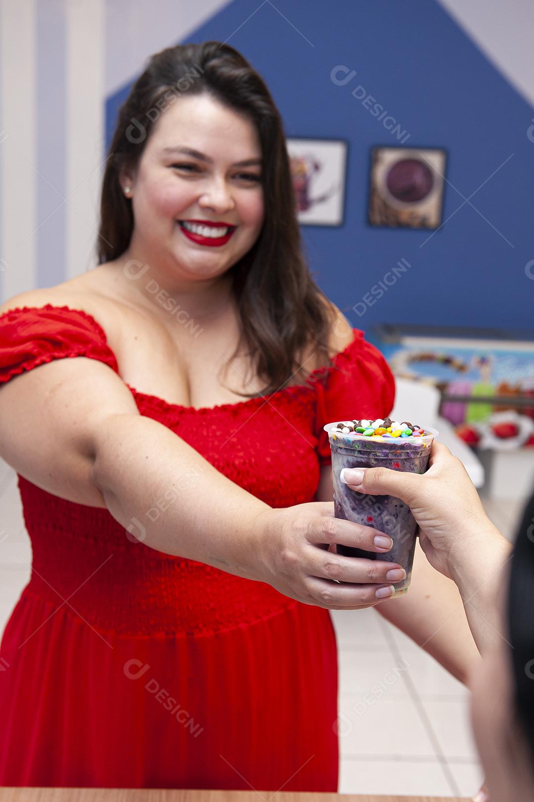 Menina bonita e sorridente recebendo um copo de açaí congelado