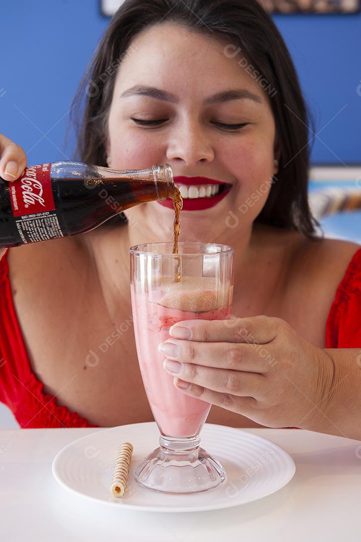 Menina bonita e sorridente tomando uma xícara de sorvete com coca cola