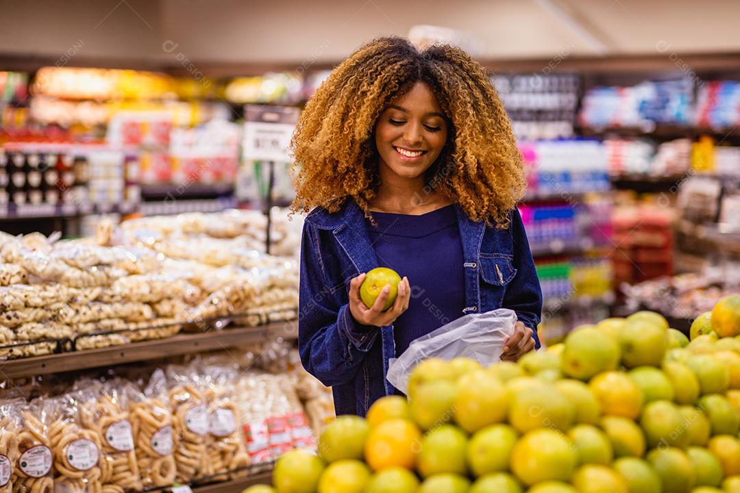 Jovem afro fazendo compras no supermercado hortifruti empurrando carrinho de compras