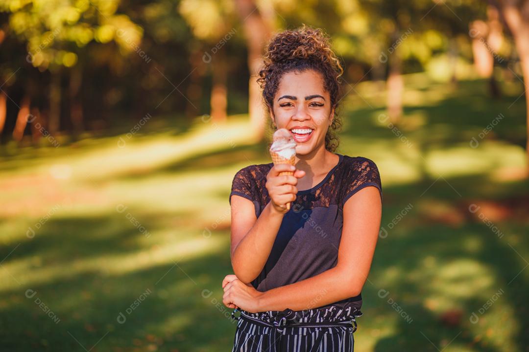 Mulher afro feliz tomando sorvete no parque.