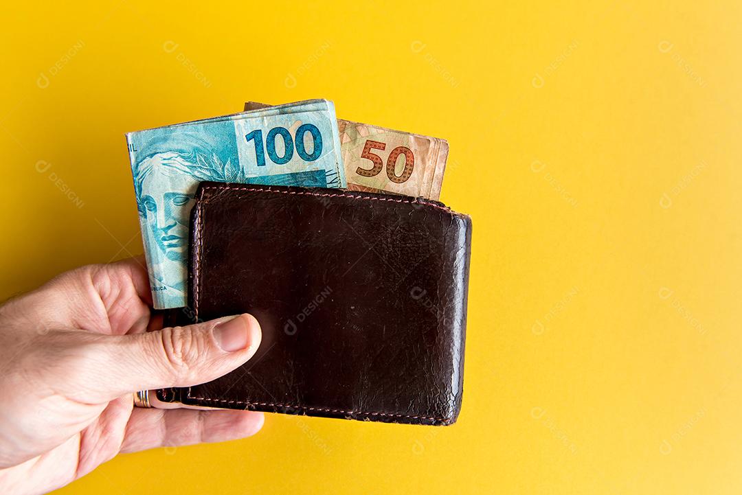 Mão segurando a carteira com dinheiro brasileiro, notas reais brasileiras