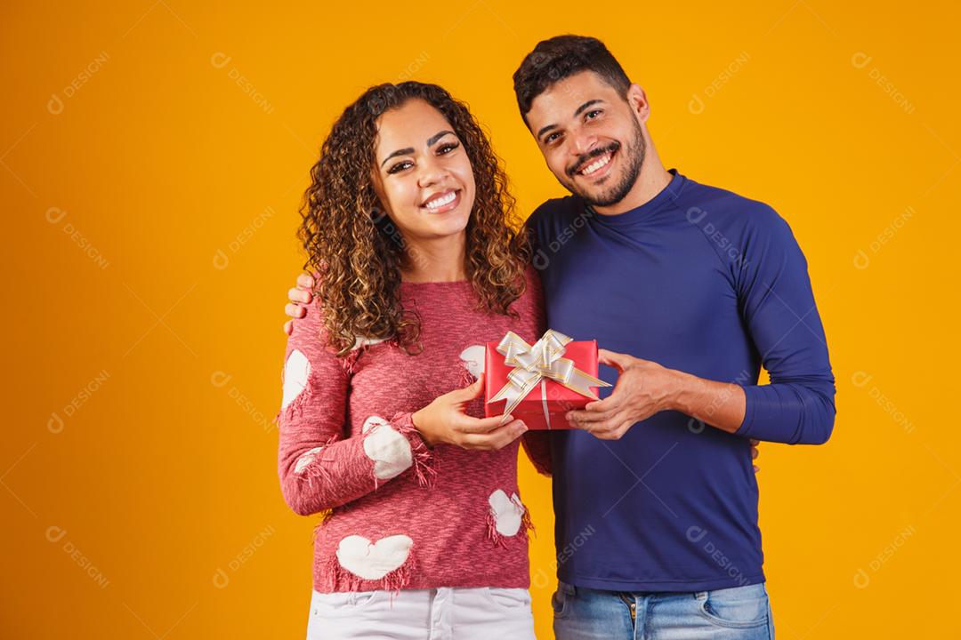 Retrato de um lindo casal em fundo amarelo com um presente