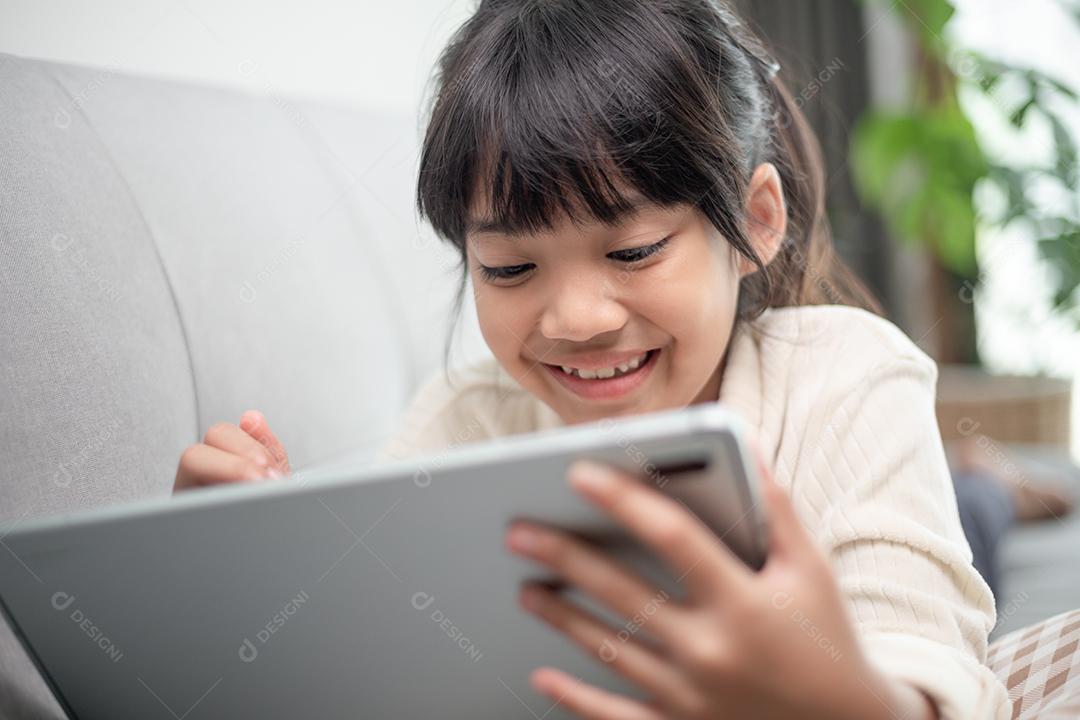 Sorridente menina deitada no sofá confortável, gostando de jogar jogo  online no computador tablet digital. viciado em tecnologia, criança feliz  usando aplicativos engraçados, informações de navegação na web.