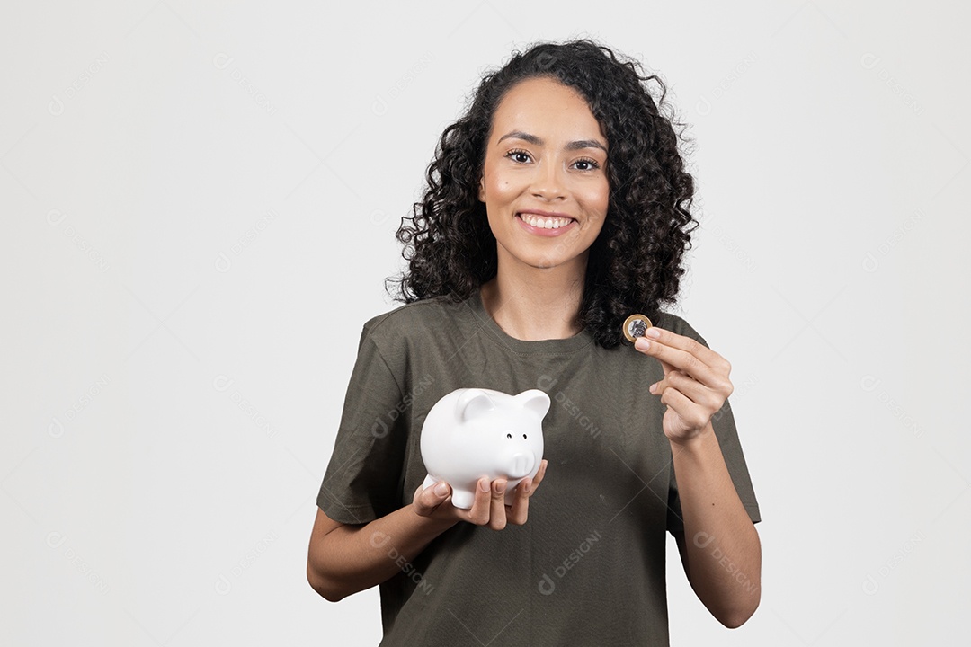 Linda mulher jovem cabelo cacheado sorridente segurando moeda de 1 real cofrinho sobre fundo branco
